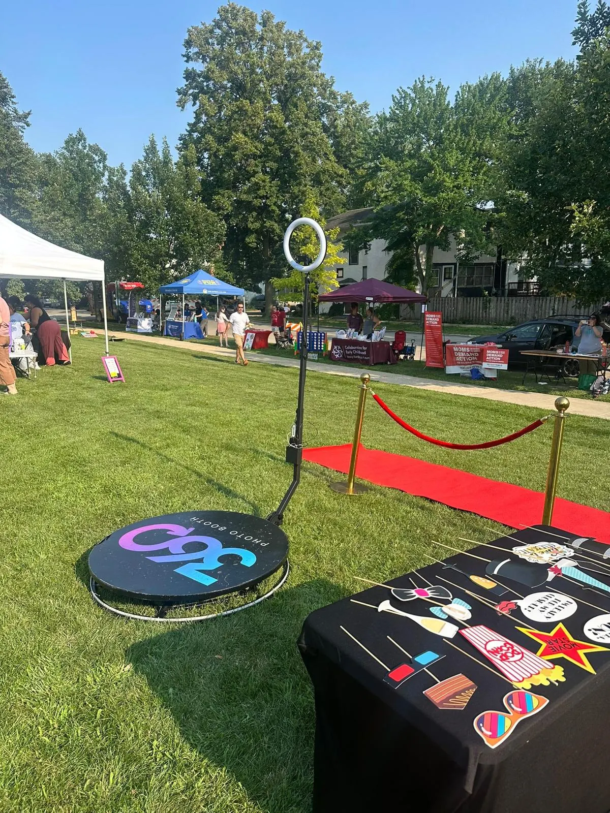 360 photo booth with a red carpet and prop table on a lawn