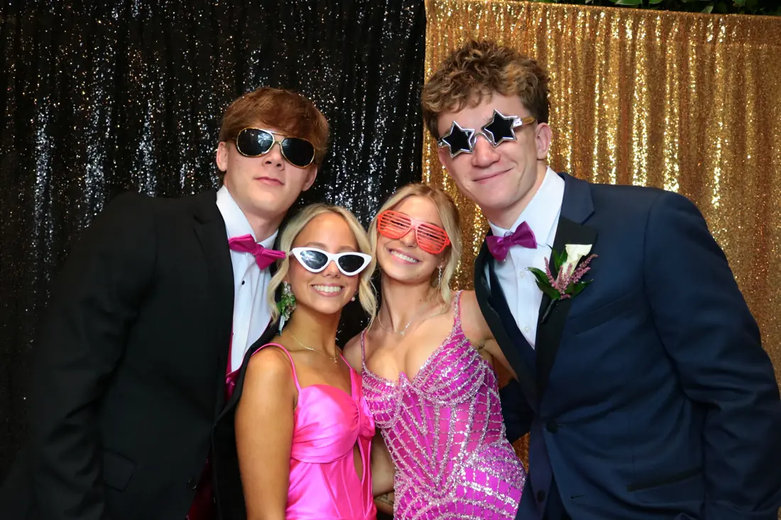 Four friends in party sunglasses in front of a sequin backdrop